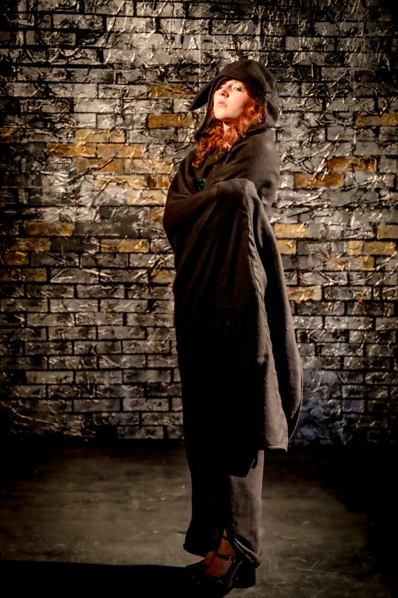 Person wearing a long coat and hat against a textured brick wall.
