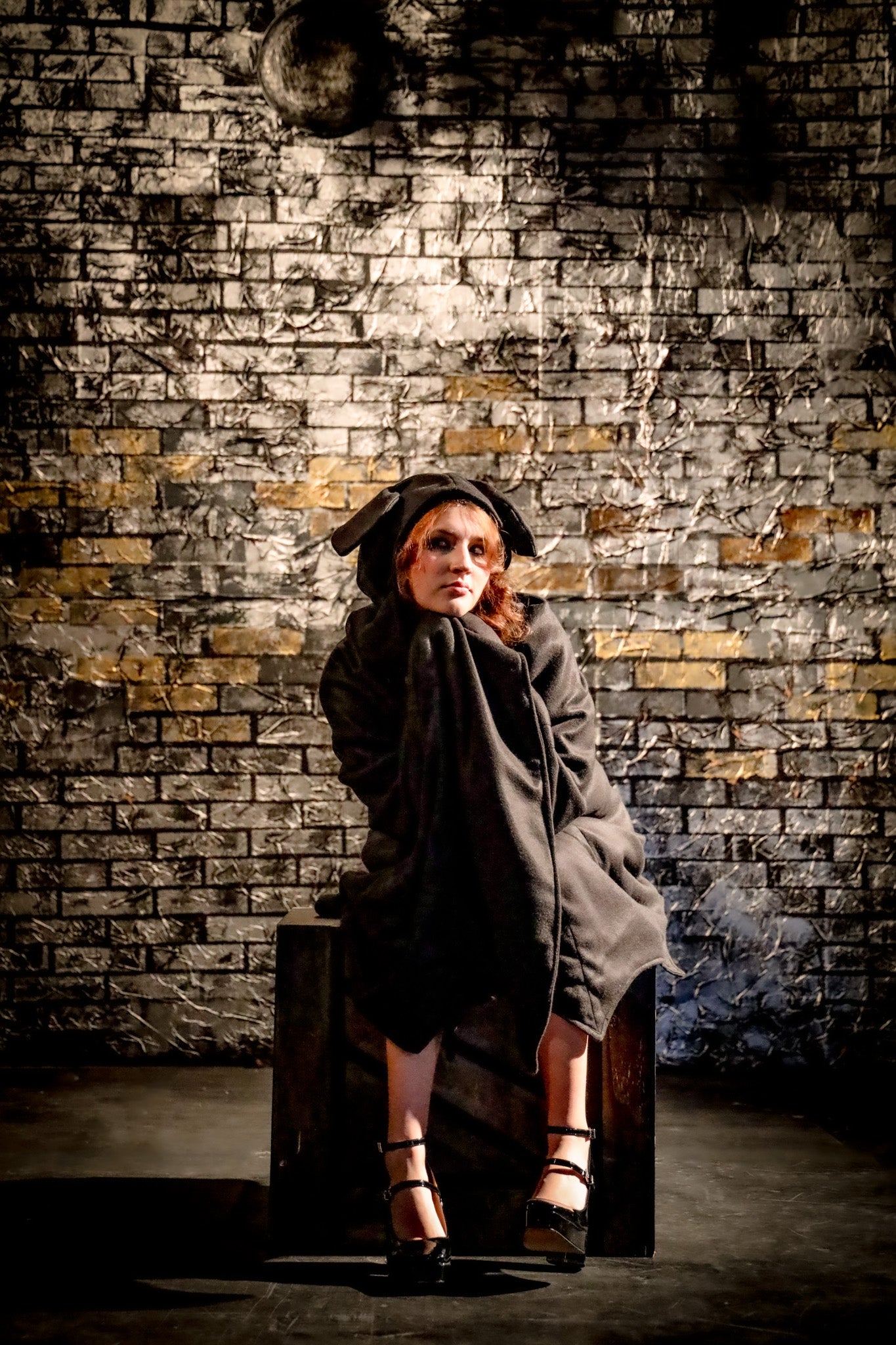 Person wearing a coat and hat against a textured brick wall.
