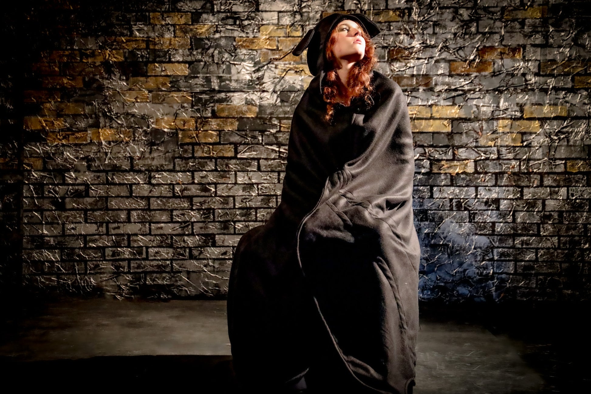 Person wrapped in a blanket against a textured brick wall