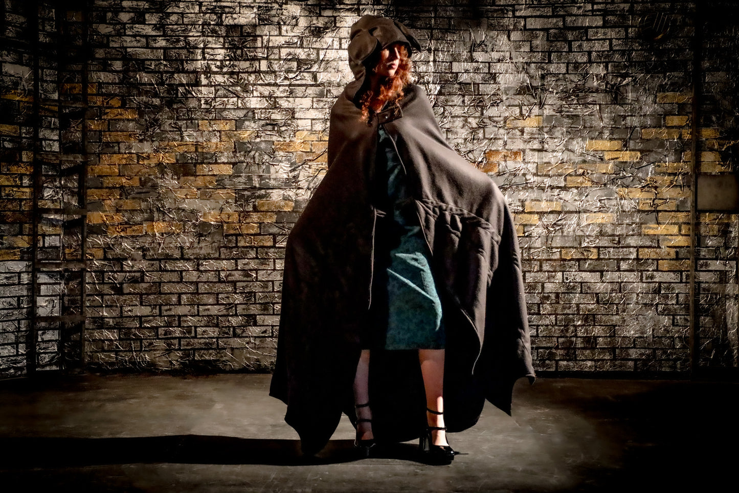 Person wearing a long coat and hat against a textured brick wall.