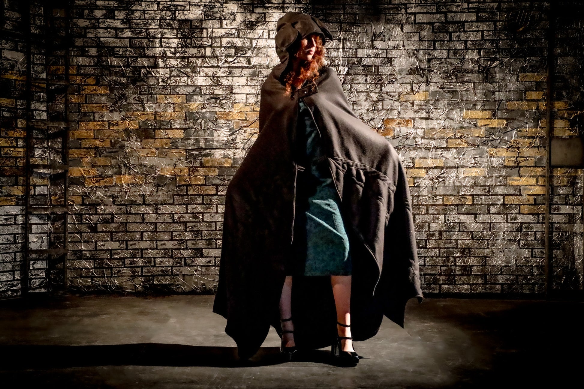 Person wearing a long coat and hat against a textured brick wall.