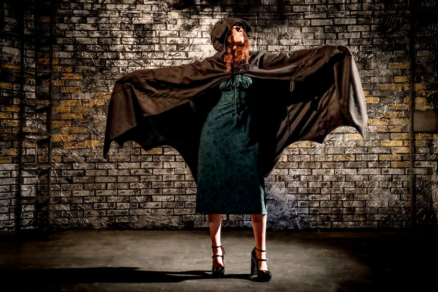 Person wearing a cape in front of a brick wall