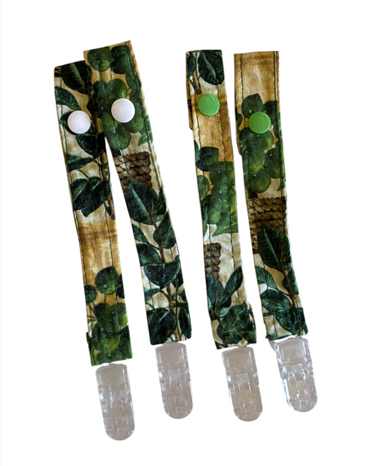 Two green camouflage-patterned pacifier straps with snaps on a white background