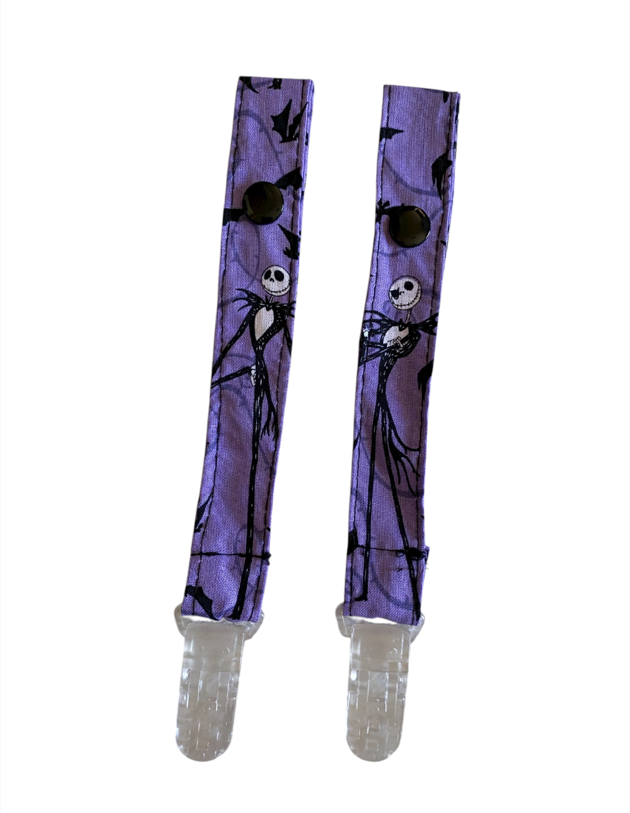 Pair of purple pacifier clips with Jack Skellington design on a white background