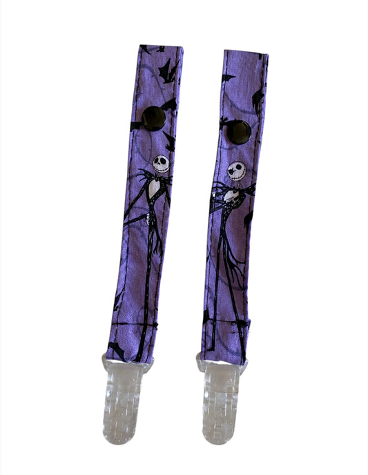 Pair of purple pacifier clips with Jack Skellington design on a white background