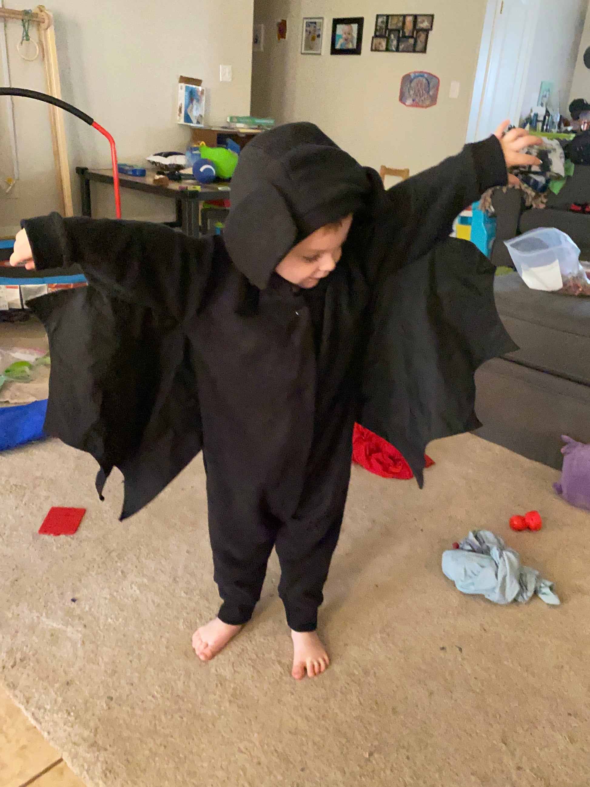 Person wearing a black hoodie and pants on a carpeted floor with toys scattered around.